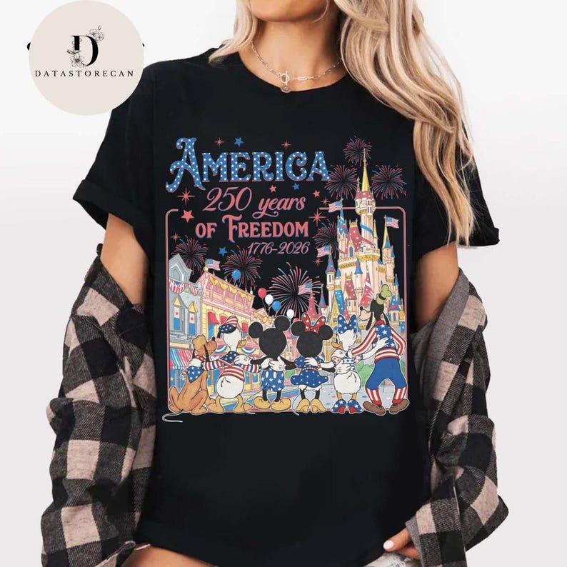 May include: Black t-shirt with a colourful graphic celebrating "America 250 years of Freedom 1776-2026." The design features fireworks, a castle, and cartoon characters. The shirt is a crew neck.