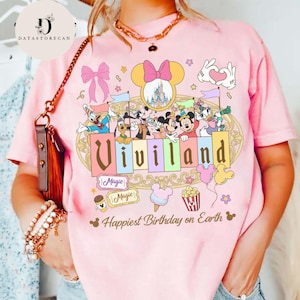 以下が含まれることがあります： 「Viviland」の文字とディズニーキャラクターが描かれたピンク色のTシャツ。ミッキーとミニー、お城、そして「Happiest Birthday on Earth」のフレーズが含まれています。その他、様々なディズニーをテーマにしたグラフィックも特徴です。