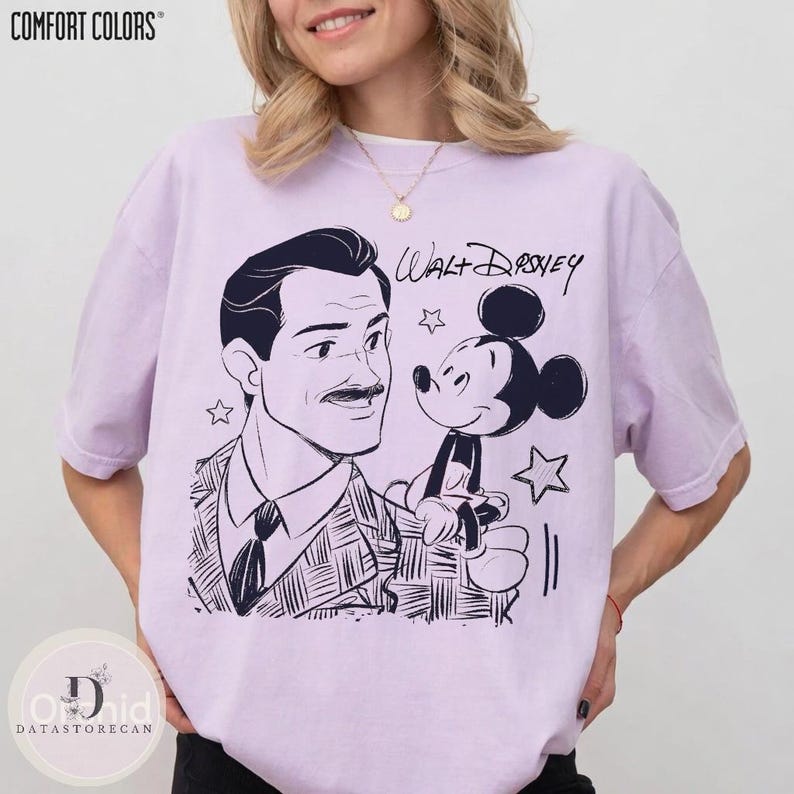 May include: A light purple t-shirt featuring a black and white illustration of Walt Disney and Mickey Mouse. The text "Walt Disney" is written above Mickey Mouse. The shirt has the Comfort Colors logo at the top left.