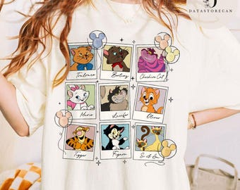May include: A white t-shirt with a graphic print of Disney characters from the animated films The Aristocats and The Lion King. The characters are arranged in a grid of Polaroid-style frames with Mickey Mouse ears and balloons. The text below each character includes their names: Toulouse, Berlioz, Cheshire Cat, Marie, Lucifer, Oliver, Tigger, Figaro, and Si & Am.