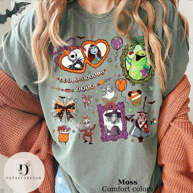 Pu&ograve; includere: T-shirt verde muschio con personaggi dei cartoni animati colorati e la scritta "BOOSH". Il design include ritratti incorniciati, palloncini e altre grafiche a tema Halloween. La maglietta &egrave; un colore comfort.
