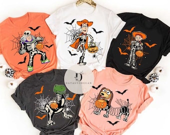 May include: Five Halloween t-shirts in orange, white, black, charcoal grey, and peach. Each shirt features a cartoon character skeleton design with a spider web, bats, and a pumpkin. Characters include Buzz Lightyear, Woody, Jessie, a dinosaur, and Slinky Dog.