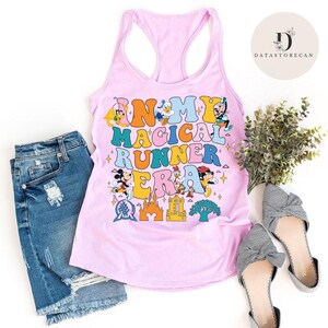 K&ouml;nnte beinhalten: Pinkes Tanktop mit einer bunten Grafik, auf der "In My Magical Runner Era" mit verschiedenen Disney-Charakteren steht. Das Tanktop wird mit Jeans-Shorts und gestreiften Schleifenschuhen kombiniert.