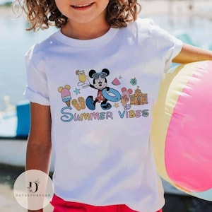 May include: White t-shirt with a colorful graphic of Mickey Mouse on a beach vacation. The graphic includes Mickey Mouse holding a drink, wearing sunglasses and a swimsuit, and a beach umbrella. The text "Summer Vibes" is written below the graphic.