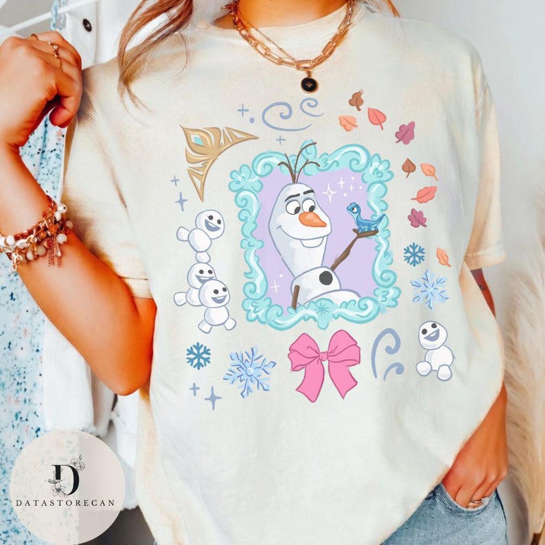Peut inclure: T-shirt cr&egrave;me avec une illustration encadr&eacute;e d'Olaf de La Reine des Neiges, tenant un oiseau bleu. Le motif comprend des flocons de neige, un n&oelig;ud rose et de petits bonhommes de neige. Le t-shirt a un effet tie-dye.