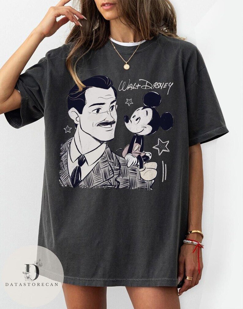 May include: Dark gray t-shirt featuring a black and white illustration of Walt Disney with Mickey Mouse. The shirt has the text "Walt Disney" in a handwritten style above the cartoon characters. The shirt is a relaxed fit.