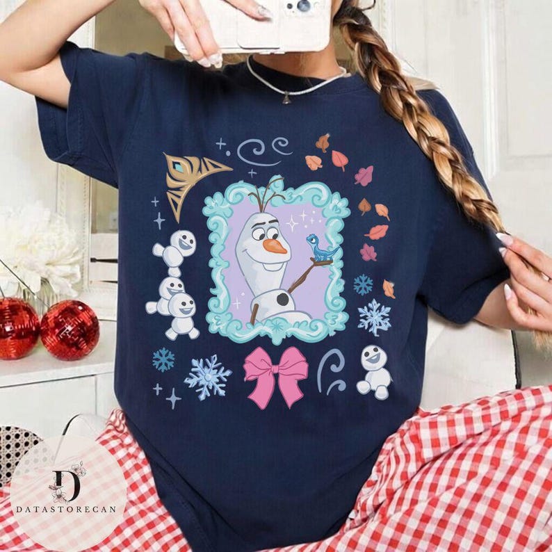 Peut inclure: T-shirt bleu marine avec un motif sur le th&egrave;me de La Reine des Neiges, repr&eacute;sentant Olaf, un oiseau bleu et des flocons de neige dans un cadre. Le motif comprend &eacute;galement un n&oelig;ud rose et d'autres &eacute;l&eacute;ments d&eacute;coratifs. V&ecirc;tement d&eacute;contract&eacute; et confortable.