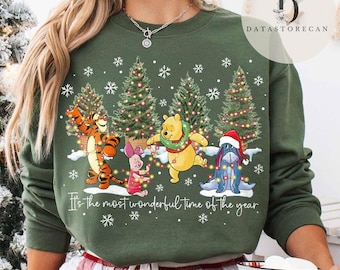 Könnte beinhalten: Grünes Sweatshirt mit einem weihnachtlichen Design mit Zeichentrickfiguren, Weihnachtsbäumen und Schneeflocken. Der Text "It's the most wonderful time of the year" ist auf der Vorderseite aufgedruckt. Das Sweatshirt hat einen Rundhalsausschnitt.