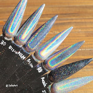 Op de afbeelding: Een set van zeven iriserende holografische nagellakken in verschillende tinten zilver en grijs. De poeders zijn gelabeld met namen zoals "3D Disco Nu", "Prism", "RB", "Razzle" en "5".