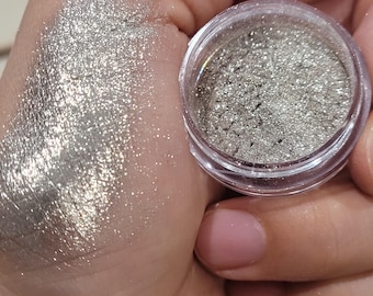 May include: A small jar of silver glitter with a light shimmer. The glitter is loose and has a fine texture.