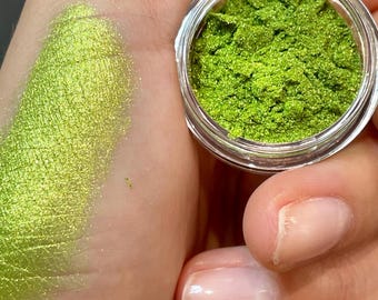 May include: A small jar of green glitter eyeshadow. The glitter is a fine, shimmery green with a metallic finish.