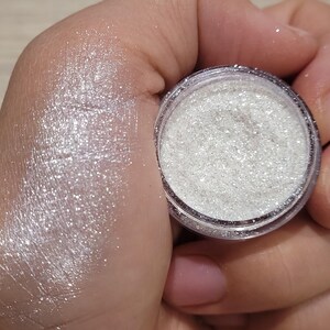 May include: A small jar of white glitter with a silver shimmer. The glitter is loose and has a fine texture.