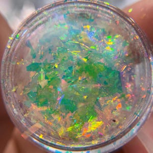May include: A clear jar filled with iridescent green and gold glitter. The glitter is loose and appears to be made of small, flat pieces.