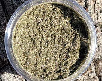 Könnte beinhalten: Ein kleines Glas gefüllt mit feinem, glitzerndem grünem Glitter. Der Glitter hat einen dezenten goldenen Schimmer.
