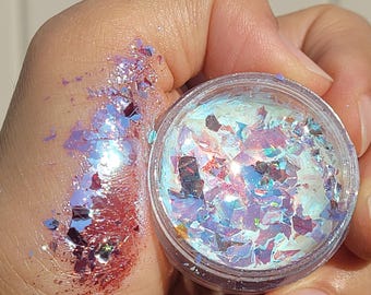 May include: A small clear jar filled with iridescent holographic glitter flakes. The glitter is a mix of blue, pink, and purple.