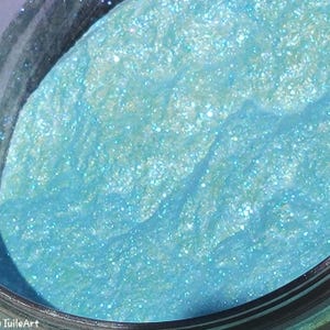 May include: A close-up of a jar of light blue glitter with a shimmery finish.