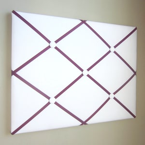May include: White cork board with a grid pattern of burgundy ribbon and white buttons.