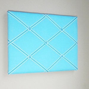 May include: A light blue fabric bulletin board with white criss-cross ribbon and clear plastic push pins.