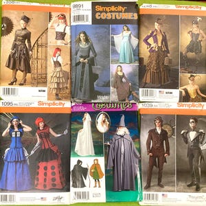 May include: A collection of six Simplicity sewing pattern envelopes featuring various costume designs, including historical, fantasy, and character-inspired outfits. Each envelope displays photographs of finished garments, model numbers, and barcodes on a green surface.