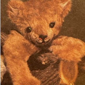 May include: A brown teddy bear with a sweet expression, sitting on a piece of wood. The bear has a long, fluffy body and a short, fluffy tail.