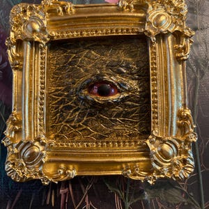 Black and gold eye sculpture wall art in gold frame