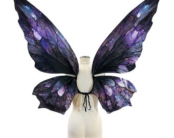 May include: A pair of purple and black butterfly wings with a galaxy print. The wings are attached to a white dress form.