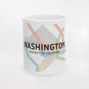 May include: White ceramic mug featuring a colorful map design of the Washington, D.C. metro system. The mug displays the city's name and "District of Columbia" in black text. The design includes lines in orange, green, blue, and yellow.