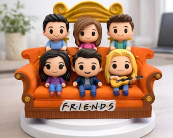 Op de afbeelding: Een verzameling beeldjes met zes stripfiguren uit de tv-serie "Friends". De figuren zijn geplaatst op een oranje bank, met het logo van de serie. De bank staat op een witte basis. De figuren dragen verschillende outfits.