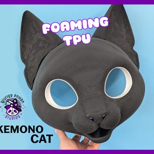 May include: A black cat mask featuring large eye openings with white rims, pointed ears, and a molded snout. The text FOAMING TPU is printed above the mask, and the text KEMONO CAT is printed below, alongside a Stuffed Panda Studios logo.