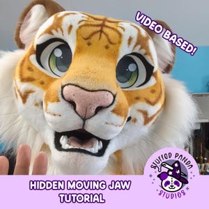 May include: A close-up of a tiger fursuit head with a moving jaw. The head is primarily orange and white, with large green eyes and a pink nose. The text "VIDEO BASED!" and "HIDDEN MOVING JAW TUTORIAL" are visible. The logo for Stuffed Panda Studios is also present.