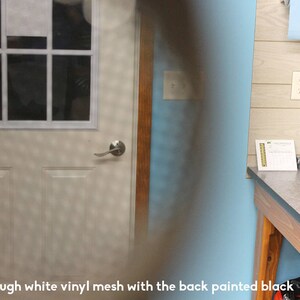 May include: A white door with a window pane and a silver door handle. The door is seen through a white vinyl mesh with the back painted black.