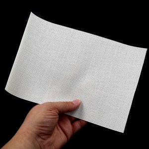 May include: A white mesh fabric with a fine grid pattern. The fabric is held in a hand.