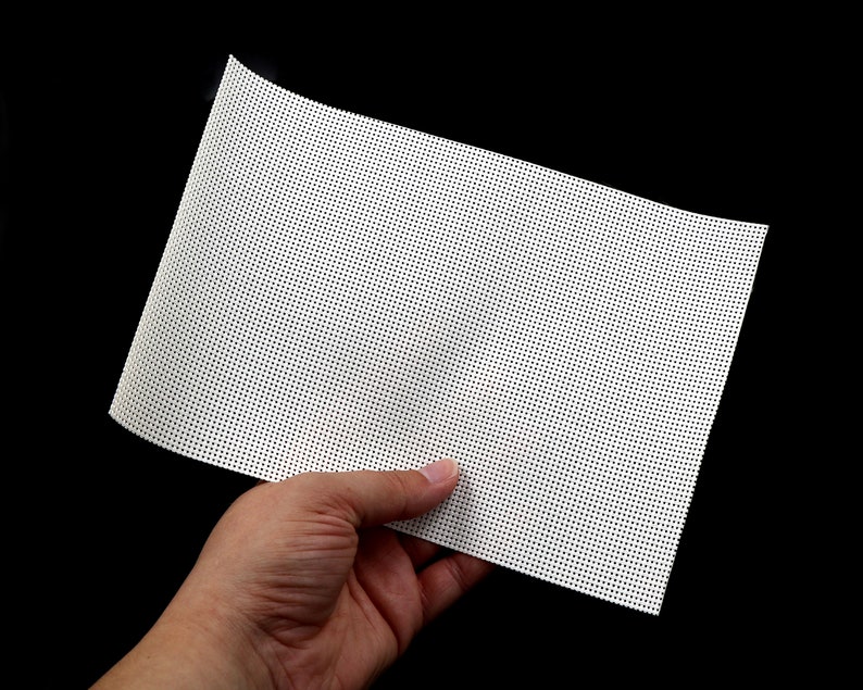 May include: A white mesh fabric with a fine grid pattern. The fabric is held in a hand.