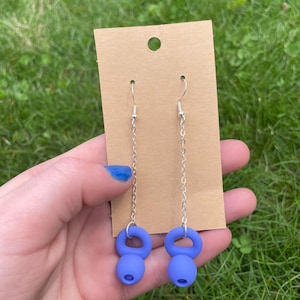 May include: A pair of drop earrings featuring silver-toned metal chains attached to matte blue kettlebell-shaped charms. The earrings are displayed on a rectangular brown cardboard backing card with a circular hole at the top for hanging.