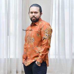 Peut inclure: Une chemise orange à manches longues avec un motif floral et géométrique détaillé. La chemise a un col boutonné et une poche poitrine. Le texte "TronicCraft" est visible sur la chemise.