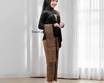 May include: A woman wearing a black long-sleeved top, patterned skirt, and head covering. The skirt and shawl feature a brown and orange batik design. A gold-colored brooch adorns the top. The text "TronicCraft" is visible on the left.