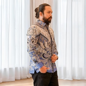 May include: A button-down shirt with a batik pattern in shades of blue, white, and brown. The shirt features an intricate design with floral and bird motifs. The text "TronicCraft" is visible on the shirt.