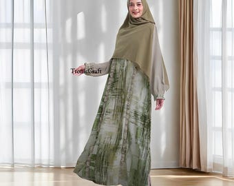 May include: A woman wearing a long, green and white patterned dress with a long-sleeved, light brown top and a matching headscarf. The dress has a ruffled hem and the top has a gathered sleeve.