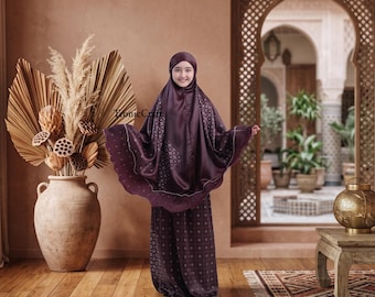 May include: A dark purple prayer garment featuring a subtle geometric pattern and a matching head covering. The fabric has a slight sheen, and the garment drapes loosely over the body, extending to the floor with a wide, flowing silhouette.