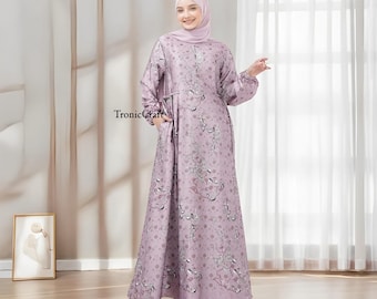 May include: A long, flowing lavender dress with a floral print and a cinched waist. The dress has long sleeves with a gathered detail at the cuffs. The model is wearing a matching lavender headscarf.