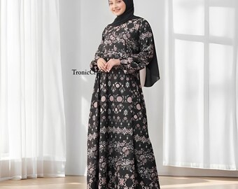 May include: A black maxi dress with a pink and white floral pattern. The dress has long sleeves and a round neckline. The dress is worn by a person wearing a black headscarf.