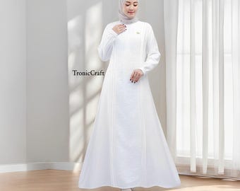 May include: A white maxi dress with long sleeves and a delicate floral pattern. The dress has a high neckline and a flowing skirt. The model is wearing a white headscarf.