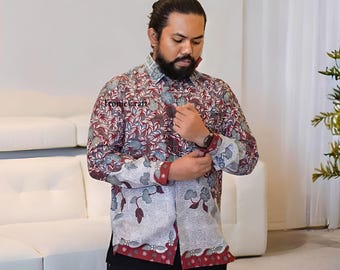 May include: A long-sleeved button-down shirt with a floral pattern in burgundy, white, and teal. The shirt has a contrasting white and burgundy floral pattern on the cuffs and bottom hem. The shirt is being worn.