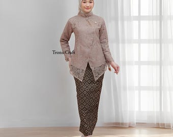 May include: A woman wearing a traditional outfit. The ensemble includes a light brown lace top with a high collar and a decorative pin, paired with a long, patterned skirt. The outfit is completed with a matching head covering. The text "TronicCraft" is visible.