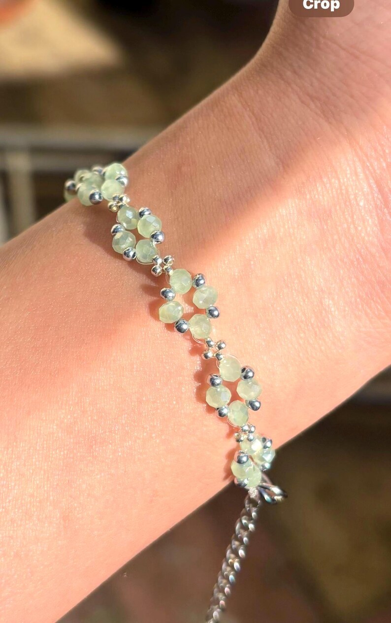 May include: A delicate bracelet featuring pale green gemstone beads and small silver-coloured accents. The bracelet is composed of multiple floral-like clusters, connected by a silver chain. Sage green, dainty, elegant, floral, handmade jewellery bracelet, gift for her, anniversary gift, frienship bracelet, floral beaded handmade jewellery, pretty bracelet, pastel jewellery bracelet, gifts for her, bestseller