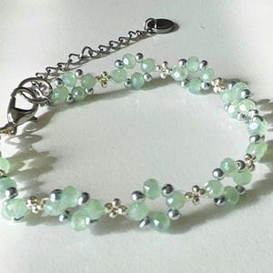 May include: A delicate bracelet featuring light green faceted beads and small silver-coloured beads. The bracelet has a silver-tone chain and clasp for adjustable sizing. The design incorporates small, decorative gold-coloured accents. Sage green, dainty, elegant, floral, hsndmade jewellery bracelet, guft for her, anniversary gift, frienship braceler, floral beaded handmade jewellery, pretty bracwlet, pastel jewellery bracelet, gifts for her, bestseller.
