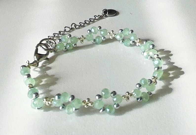 May include: A delicate bracelet featuring light green faceted beads and small silver-coloured beads. The bracelet has a silver-tone chain and clasp for adjustable sizing. The design incorporates small, decorative gold-coloured accents. Sage green, dainty, elegant, floral, hsndmade jewellery bracelet, guft for her, anniversary gift, frienship braceler, floral beaded handmade jewellery, pretty bracwlet, pastel jewellery bracelet, gifts for her, bestseller.