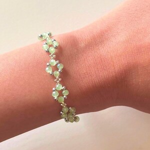 May include: A bracelet with light green beads and silver-coloured details. The beads are arranged in a repeating pattern, creating a stylish accessory. The bracelet is shown on a wrist, showcasing its design and colour. Sage green, dainty, elegant, floral, handmade jewellery bracelet, gift for her, anniversary gift, frienship braceler, floral beaded handmade jewellery, pretty bracwlet, pastel jewellery bracelet, gifts for her, bestseller