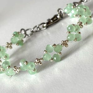 May include: A delicate bracelet featuring light green, faceted beads strung together with silver-toned metal. The bracelet has a chain closure and small decorative silver accents between the beads. The beads are a soft, pastel green colour. Sage green, dainty, elegant, floral, hsndmade jewellery bracelet, guft for her, anniversary gift, frienship braceler, floral beaded handmade jewellery, pretty bracwlet, pastel jewellery bracelet, gifts for her, bestseller