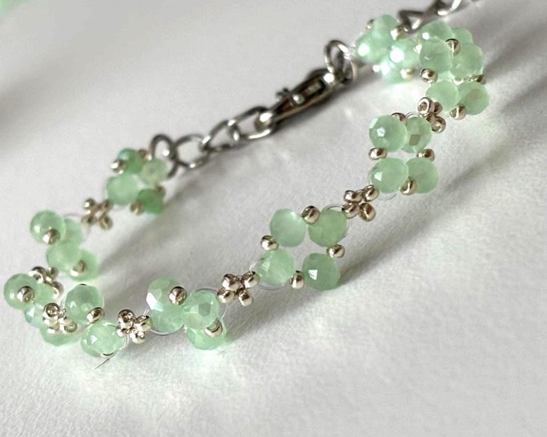 May include: A delicate bracelet featuring light green, faceted beads strung together with silver-toned metal. The bracelet has a chain closure and small decorative silver accents between the beads. The beads are a soft, pastel green colour. Sage green, dainty, elegant, floral, hsndmade jewellery bracelet, guft for her, anniversary gift, frienship braceler, floral beaded handmade jewellery, pretty bracwlet, pastel jewellery bracelet, gifts for her, bestseller